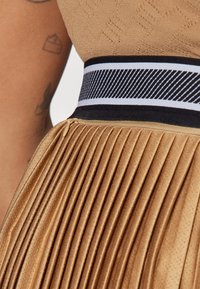 Tan-färgad plisserad tyg med en slät yta, med en kontrasterande svart och vit randig midja och med en dragkedja på sidan.