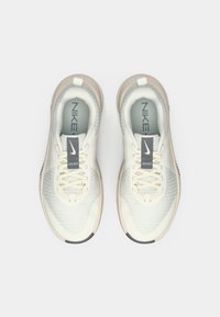 Ανοιχτό μπεζ αθλητικά παπούτσια με επάνω από διχτυωτό υλικό, επίπεδα κορδόνια και παχύ λευκό μεσοπάτο. Μαύρη εξωτερική σόλα και γκρι branding ορατό στη γλώσσα.