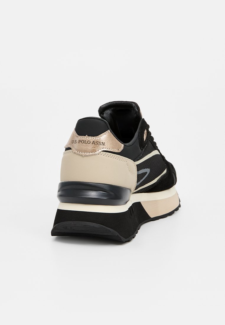 Zapatilla deportiva negra y beige con paneles de malla, suela de goma y detalle del logotipo en el talón, que muestra texturas y colores en capas.