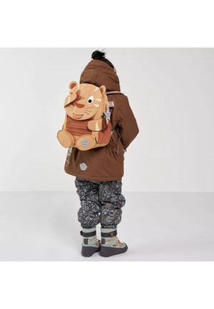 Kind trägt einen braunen Mantel und gemusterte Hosen, steht und ist von hinten zu sehen, mit einem hellbraunen, tigerförmigen Rucksack auf dem Rücken.