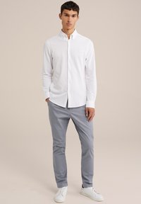 Camicia bianca button-up con colletto, maniche lunghe, abbinata a pantaloni grigi chiari e sneaker bianche. Design semplice e aderente senza motivi visibili.
