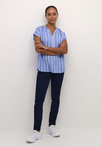 Chemise à manches courtes bleu clair avec des rayures verticales blanches et un col boutonné, accompagnée d'un jeans skinny bleu marine et de baskets blanches.