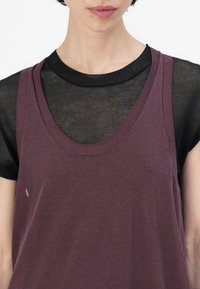 Violet mouwloos topje over een zwarte doorschijnende blouse; ronde hals, zachte stof; heeft een kleine vlek op de paarse stof.