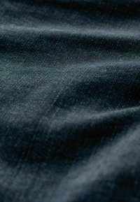Tela de mezclilla oscura que presenta una textura suave con un sutil patrón de espiga diagonal, con pliegues y un tono azul intenso.