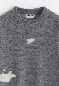 Pull en tricot gris avec col rond, présentant un motif abstrait blanc sur le devant. Texture douce, design décontracté. Étiquette de la marque visible.