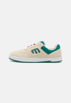 Beige velúr sneaker zöld hálós részletekkel, lapos fűzőkkel, perforált kidolgozással és fehér gumitalppal. Az oldalán logóval rendelkezik.