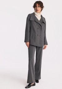 Szary wełniany płaszcz typu peacoat zapinany na podwójne guziki, z dużymi klapami, dwiema przednimi kieszeniami, w połączeniu z szarymi spodniami w kant oraz czarnymi mokasynami.