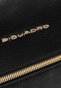 Zwarte leren tas met een getextureerd oppervlak, voorzien van een rits in goudkleur en het logo "Piquadro" in metallic letters.
