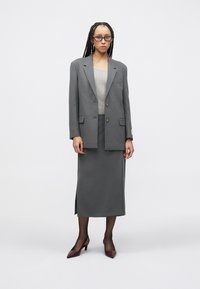 Γκρι ραμμένο σακάκι με δύο κουμπιά, σε συνδυασμό με γκρι εφαρμοστή φούστα με πλαϊνή σχισμή. Το μοντέλο φοράει μπορντό ψηλοτάκουνα και υφασμάτινο τοπ.