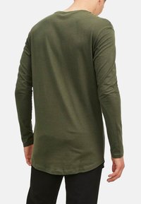Long-sleeve shirt in olive green, made of soft fabric, featuring a round neckline and a longer back hem with a smooth texture.