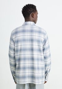 Camicia con bottoni in un tessuto leggero, caratterizzata da un motivo a quadri blu e bianchi, colletto e maniche lunghe con polsini abbottonati.