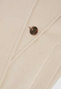 Beige wollen blend jas met een gestructureerde afwerking, scherpe revers en een enkele donkerbruine knop met zichtbaar logo.