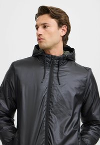 Schwarze Kapuzenjacke mit einer glatten, glänzenden Textur, durchgehendem Reißverschluss vorne und Kordelzugkapuze, mit kontrastierender Innenfarbe.