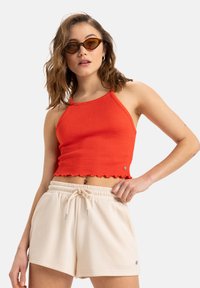 Red ribbed crop top with scalloped hem, paired with beige drawstring shorts. The ensemble features a relaxed fit and lightweight fabric.