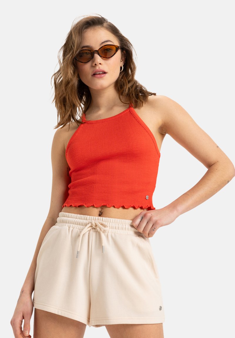 Red ribbed crop top with scalloped hem, paired with beige drawstring shorts. The ensemble features a relaxed fit and lightweight fabric.