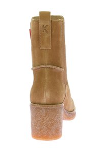 Bota de tobillo de ante color beige con tacón ancho, logo "K" en relieve en la parte trasera y costuras mínimas. Suela de goma transparente con acabado texturizado.