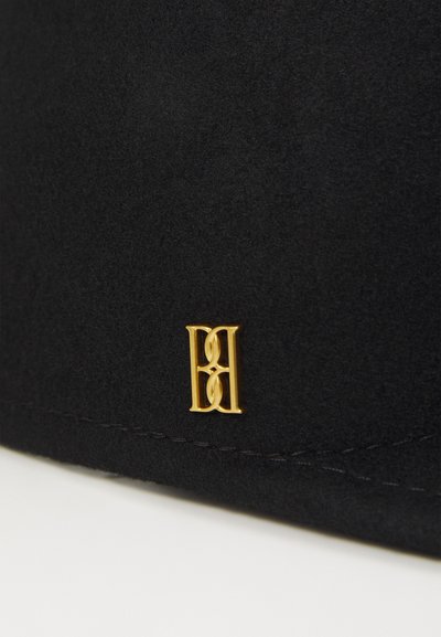 Bolso de ante negro con un destacado acento de logo dorado. La textura es suave y se pueden ver las costuras a lo largo de los bordes.