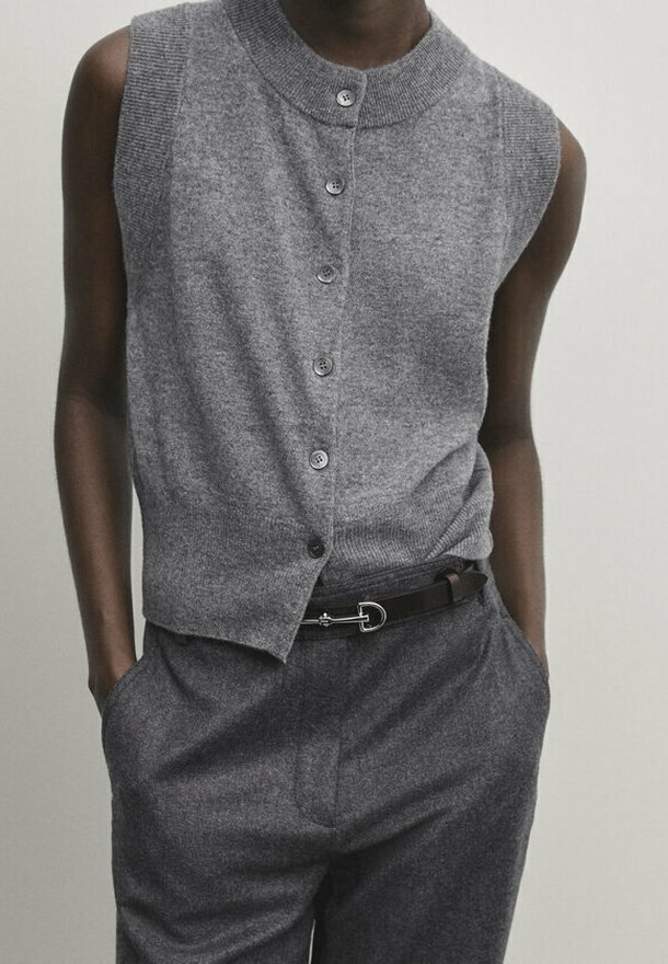 Gray sleeveless cardigan with a high collar, featuring a button front and ribbed texture, paired with gray trousers and a black belt.