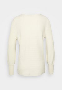Krämfärgad tröja med ribbad struktur, långa ballongärmar och vid halsringning, med en avslappnad passform och mjukt material.