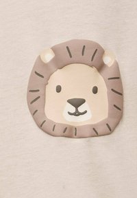 Měkká béžová tkanina má design hlavy lva v světle hnědé a smetanové barvě, s tmavými akcenty pro detaily, včetně vousů a uší.