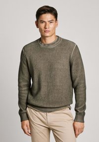 Olivengrøn ribstrikket sweater med rund halsudskæring, lange ærmer og en struktureret overflade. Har en kontrasterende stribet kant og manchetter.