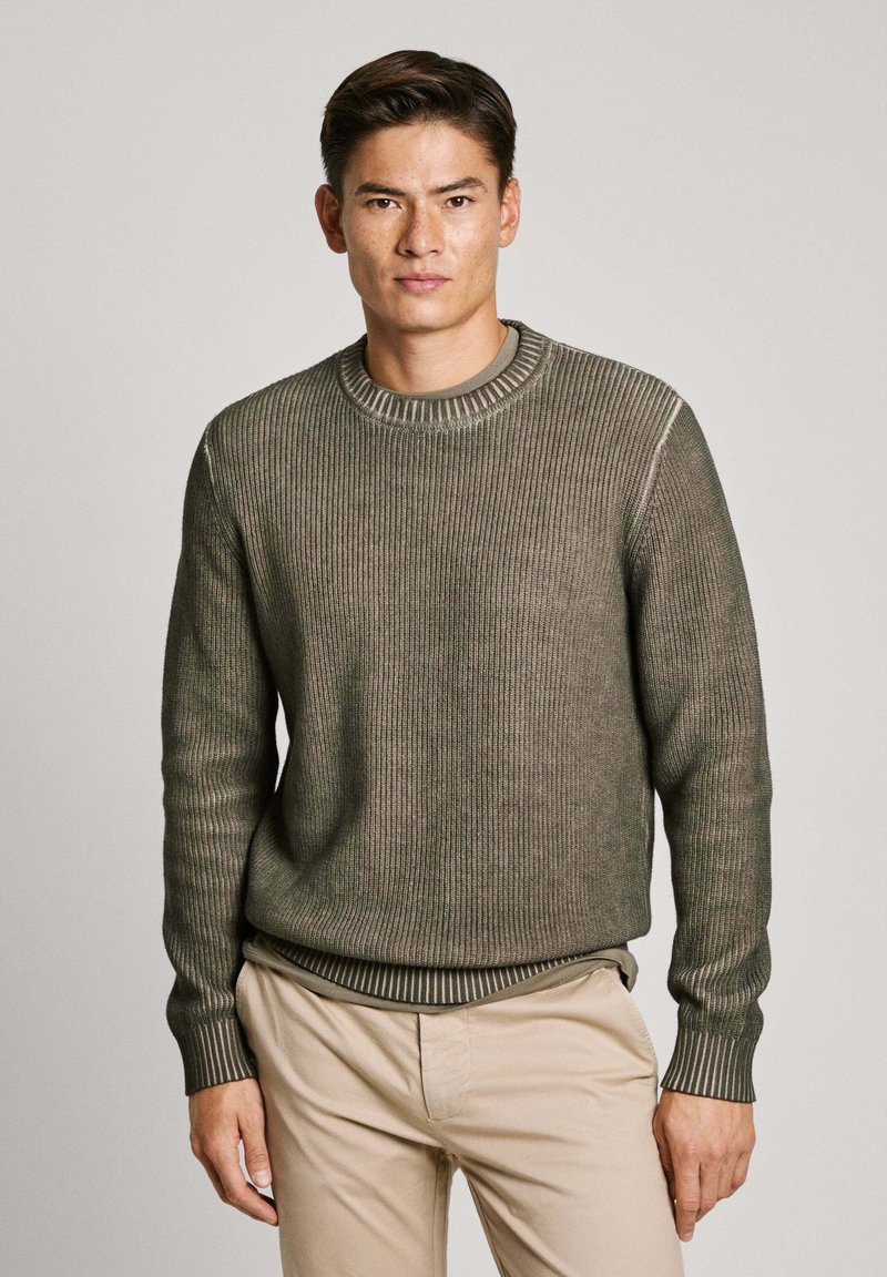Olivengrøn ribstrikket sweater med rund halsudskæring, lange ærmer og en struktureret overflade. Har en kontrasterende stribet kant og manchetter.