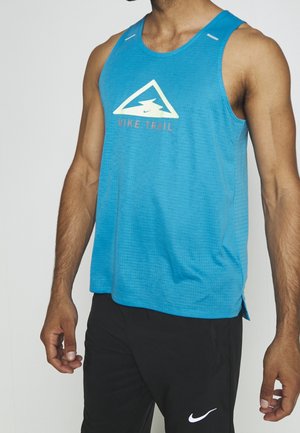 Homme portant un débardeur Nike Trail bleu et un pantalon Nike noir, debout devant un fond clair uni.