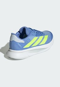 Blauwe mesh sportieve schoen met drie reflecterende gele strepen, een grijze hielkap en een getextureerde witte zool met de tekst "LIGHTMOTION".