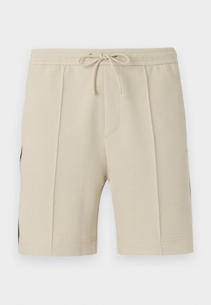 Beige teksturerte shorts med frontplissert, elastisk midjebånd og snøring, vist mot en ensfarget bakgrunn.