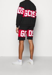 Completo composto da felpa nera e pantaloni corti con lettering rosso e bianco "GCDS". Tessuto in cotone, vestibilità comoda, blocchi di colore contrastanti su entrambi i capi.