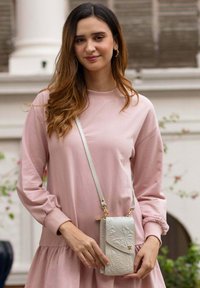 Roze oversized sweatshirt-stijl jurk met ballonmouwen, vergezeld van een textuur lichtgrijze schoudertas met bloemenpatronen.