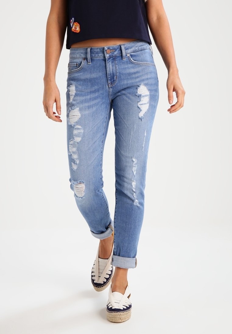 Jeans de mezclilla azul con detalles deshilachados y un corte ajustado. Puños enrollados y un leve desvanecimiento. Combinados con alpargatas blancas con acentos en azul marino.