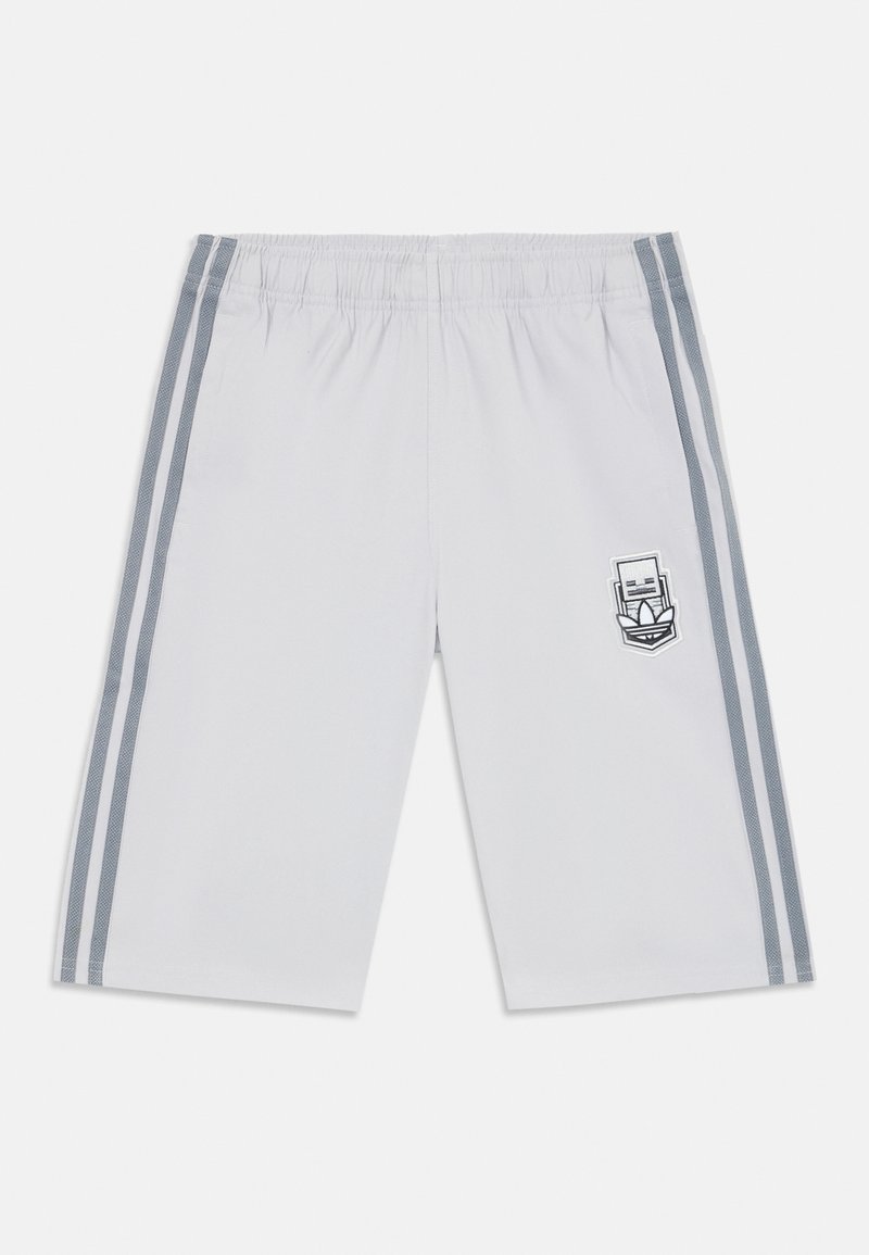 White athletic shorts with an elastic waistband, featuring two gray side stripes and a logo patch on the left leg. Smooth fabric texture.