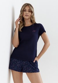 Granatowa koszulka z krótkim rękawem z małym różowym logo, w zestawie z granatowymi szortami z wielokolorowym wzorem w kropki. Miękka struktura materiału.
