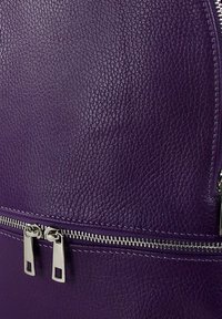 Paarse leren rugzak met een gestructureerde afwerking, voorzien van zilverkleurige hardware en een voorvak met rits. Met accentstiksels langs de naden.