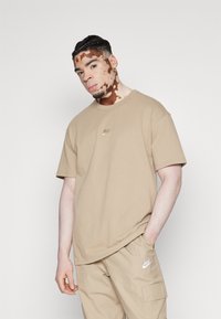 Bež majica iz bombaža s okruglim izrezom i kratkimi rokavi, ki ima na prsih majhen vezen Nike logotip. Prijetna prileganje, teksturirana tkanina.