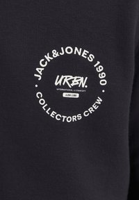 Schwarzes Sweatshirt mit einem runden weißen Logo und dem Text: "JACK&JONES 1990 URBN. INTERNATIONAL JJ CONCEPT COLLECTORS CREW."