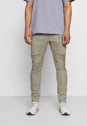 Pantaloni cargo verde oliva chiaro con più tasche, vestibilità a gamba affusolata e tessuto testurizzato. Indossati con una maglietta grigia chiara e sneakers bianche.