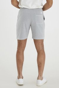 Gray cotton shorts with a drawstring waistband, featuring a back pocket and stitched hem details. Model wears white sneakers.