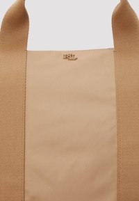 Torba iz žute tkanine s glatkom teksturom, sa zlatnim hardverom s ugraviranim logotipom i dvije čvrste naramenice.