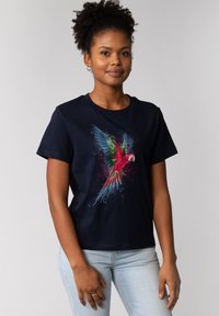 T-shirt en coton bleu marine présentant un graphique coloré de perroquet avec des éclaboussures de rouge, vert et bleu, à manches courtes et col rond.