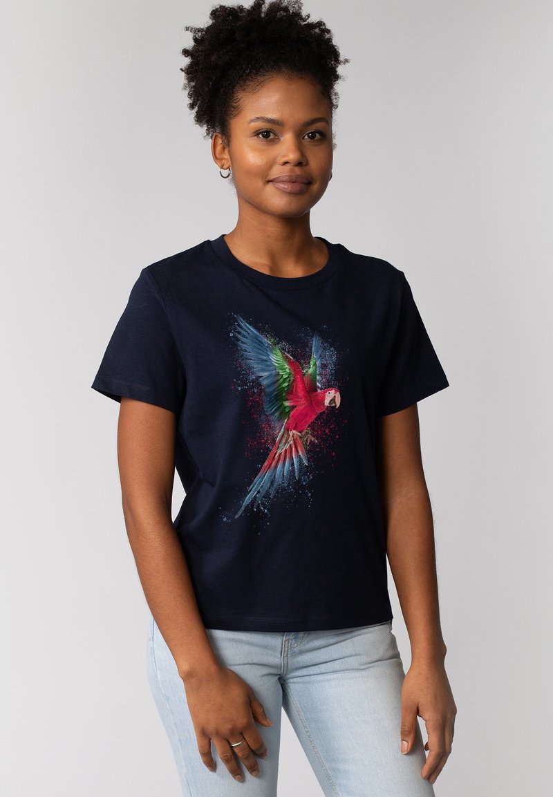 T-shirt en coton bleu marine présentant un graphique coloré de perroquet avec des éclaboussures de rouge, vert et bleu, à manches courtes et col rond.