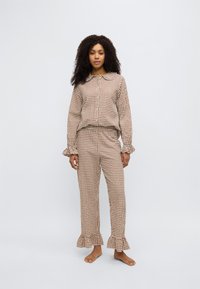 Καφέ και εκρού πιτζάμα σε καρό σχέδιο με πουκάμισο με γιακά και κουμπιά και με βολάν στα μανίκια. Το παντελόνι έχει βολάν στο τελείωμα. Κατασκευασμένο από ελαφρύ ύφασμα.