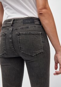 Jeans de mezclilla gris de tiro alto, con dos bolsillos traseros y una etiqueta de marca negra. La tela tiene una ligera textura deslavada.