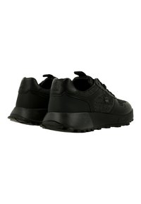 Paire de baskets basses noires en tissu texturé avec panneaux lisses, semelles épaisses, et logos de marque au talon et sur le côté, vues de dos.