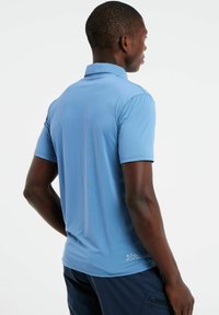 Mėlynas trumpomis rankovėmis polo marškinėlis, pagamintas iš tekstūruotos medžiagos, su stovinčiu apykakle ir logotipu šalia apatinio krašto.