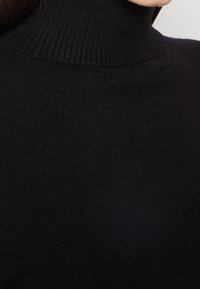 Maglione a collo alto di colore nero realizzato in morbido tessuto lavorato a maglia, con una texture a coste sul collo e sui polsini, e un design aderente.
