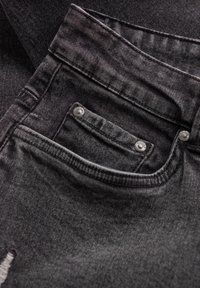 Primer plano de unos pantalones vaqueros negros que muestra el bolsillo frontal, el pequeño bolsillo para monedas con remaches de metal, y los detalles de la costura del lazo del cinturón.