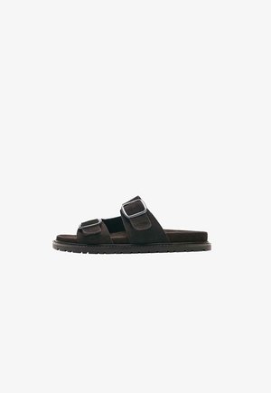 Sandalo slide in suede nero con due ampi cinturini regolabili e fibbie argentate, suola piatta con battistrada testurizzato per una migliore presa.