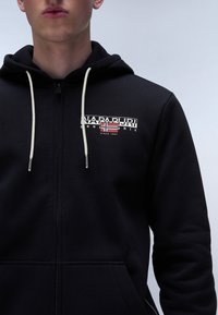 Sudadera negra con cremallera fabricada en algodón con un logo que presenta la bandera noruega. Los cordones son de color beige, con detalles de costura visibles en la tela.